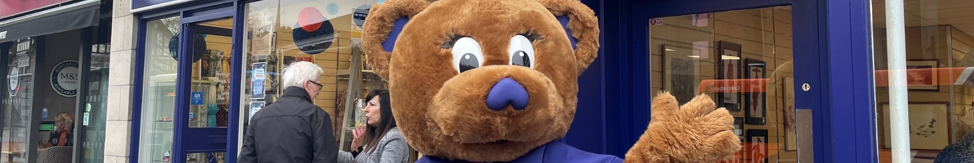 harry-the-bear-mascot-outside-hospice-shop-waving