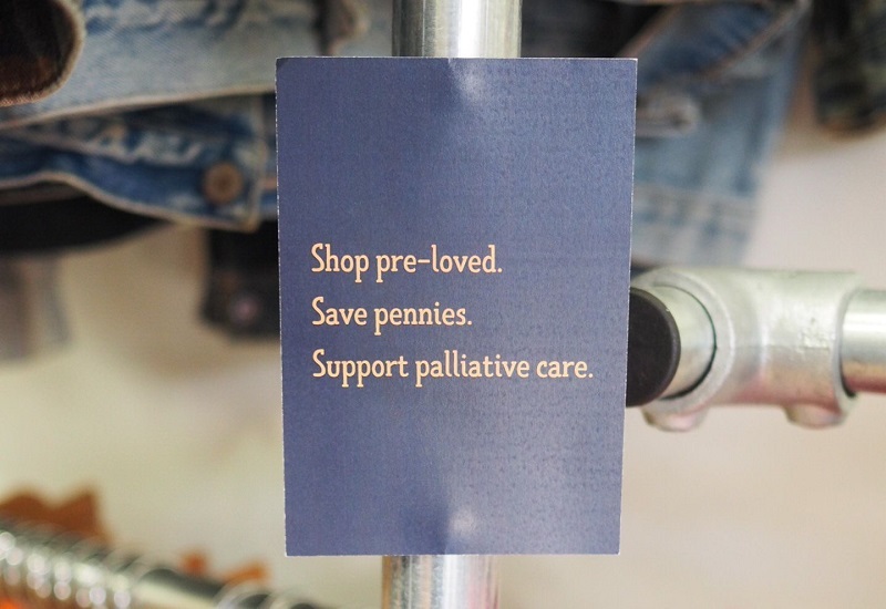 sign-on-clothes-rail-reading-shop-pre-loved-save-pennies-support-palliative-care