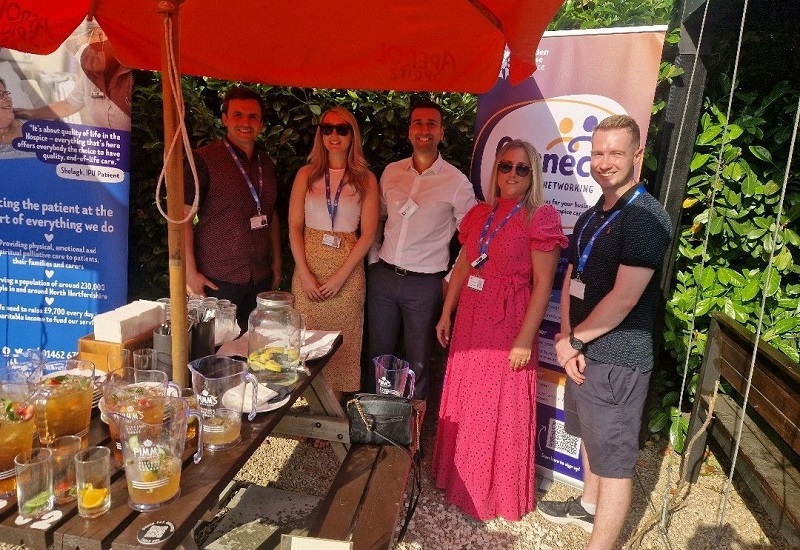 hospice-staff-stand-outside-around-a-picnic-bench-in-front-of-banners