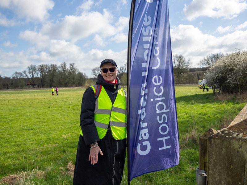 a-volunteer-smiling-standing-in-a-field-next-to-a-ghhc-flag