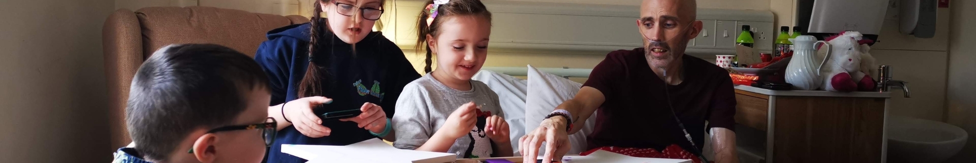 ipu-patient-sits-in-bed-with-his-children-next-to-him-making-crafts