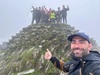 man-takes-selfie-with-group-on-mountain-peak-in-the-distance