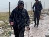 a-man-with-hiking-sticks-walks-up-mountain-in-heavy-rain