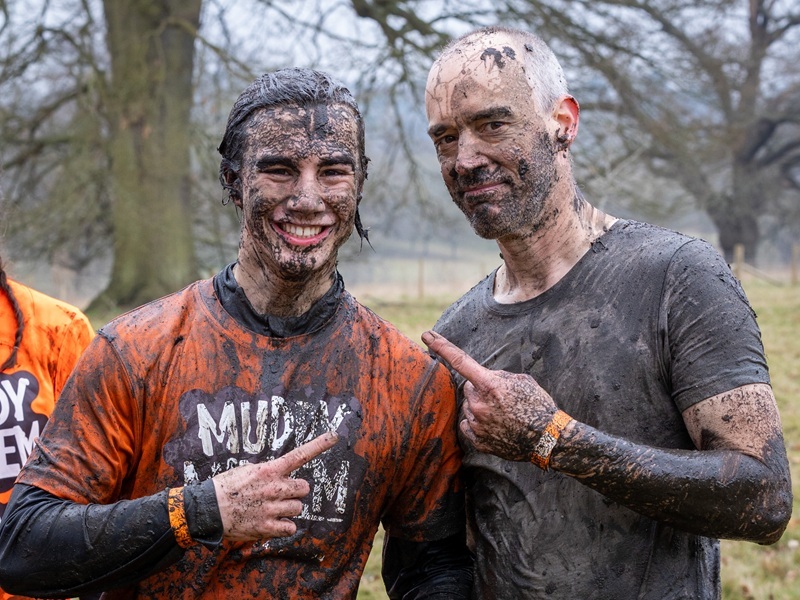 two-participants-covered-in-mud-point-at-eachother-and-smile-at-the-camera